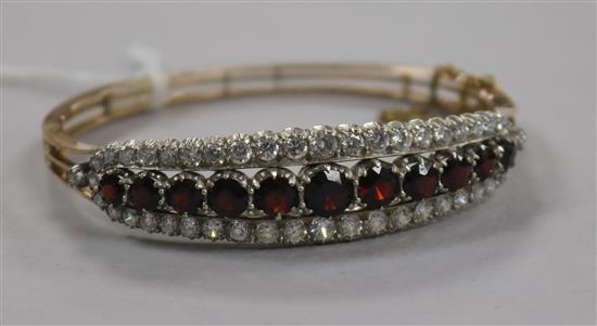 A Victorian style yellow metal, garnet and white sapphire? set hinged bangle.